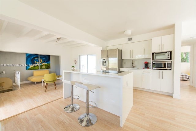 kitchen featuring beamed ceiling, sink, white cabinets, appliances with stainless steel finishes, and light hardwood / wood-style floors