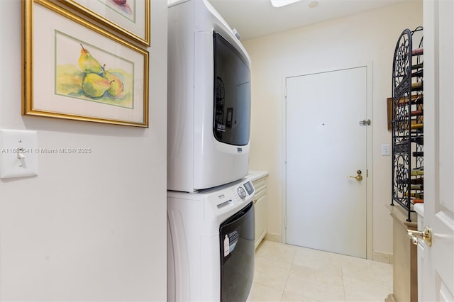 clothes washing area featuring light tile patterned flooring, cabinets, and stacked washing maching and dryer