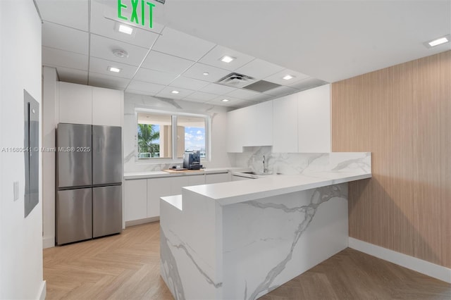 kitchen featuring a drop ceiling, kitchen peninsula, stainless steel fridge, white cabinetry, and light parquet flooring