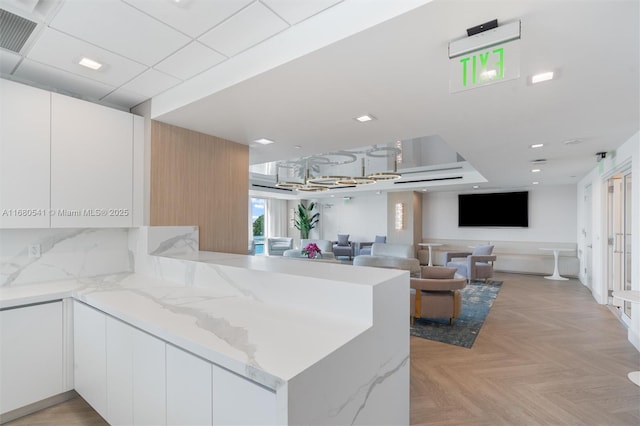 kitchen featuring kitchen peninsula, white cabinets, light stone countertops, and light parquet floors