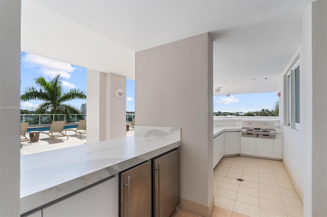 kitchen with white cabinets, light tile patterned flooring, light stone counters, and fridge