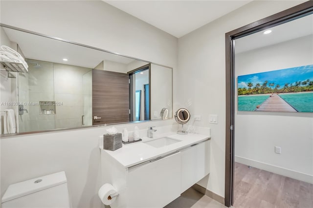 bathroom featuring toilet, hardwood / wood-style flooring, vanity, and tiled shower