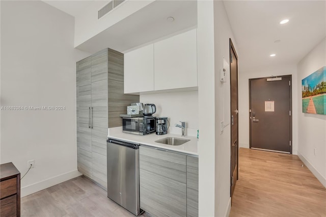 kitchen with stainless steel dishwasher, sink, light wood-type flooring, and white cabinets