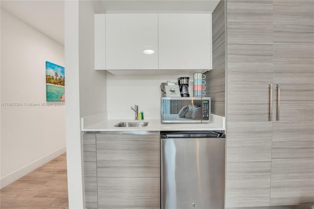 kitchen with light hardwood / wood-style floors, white cabinetry, stainless steel dishwasher, and sink