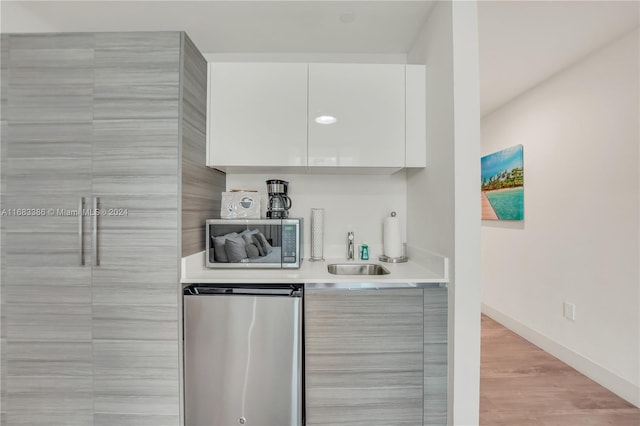 bar with white cabinetry, light hardwood / wood-style floors, sink, and stainless steel fridge