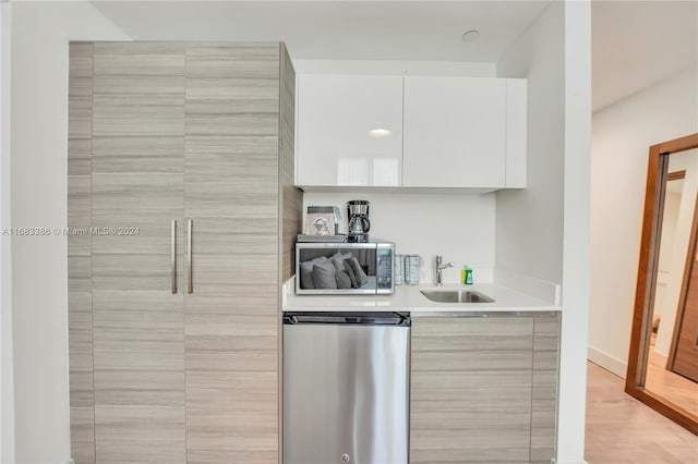 kitchen with appliances with stainless steel finishes, sink, white cabinetry, and light hardwood / wood-style flooring