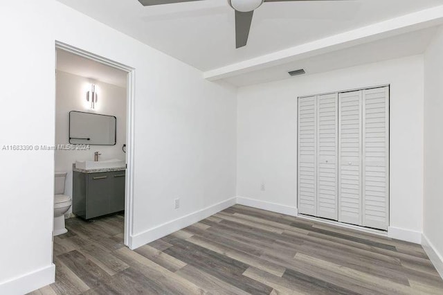 unfurnished bedroom with connected bathroom, ceiling fan, a closet, and dark wood-type flooring