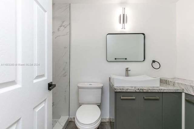 bathroom featuring vanity, hardwood / wood-style flooring, toilet, and tiled shower