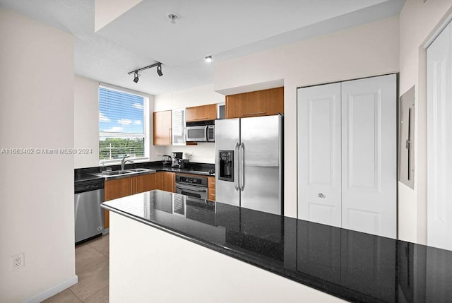 kitchen featuring track lighting, stainless steel appliances, dark stone countertops, sink, and light tile patterned floors