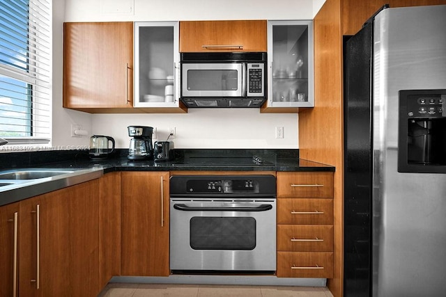 kitchen with appliances with stainless steel finishes, dark stone counters, and light tile patterned floors