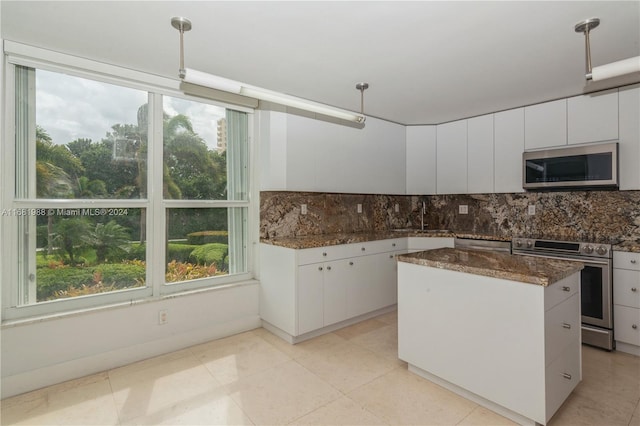 kitchen featuring stainless steel appliances, tasteful backsplash, dark stone countertops, a center island, and white cabinets