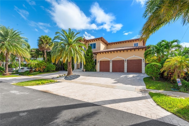 mediterranean / spanish-style home featuring a garage, stucco siding, a tile roof, and decorative driveway
