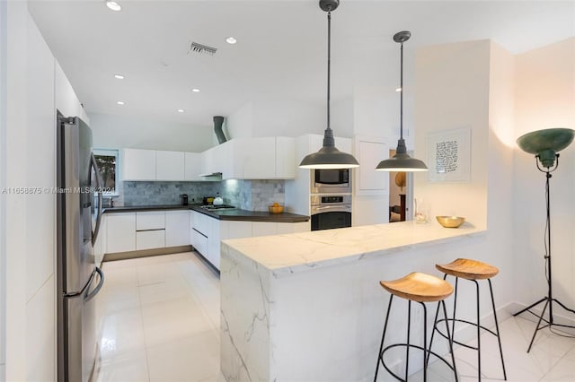 kitchen featuring white cabinetry, hanging light fixtures, backsplash, kitchen peninsula, and appliances with stainless steel finishes