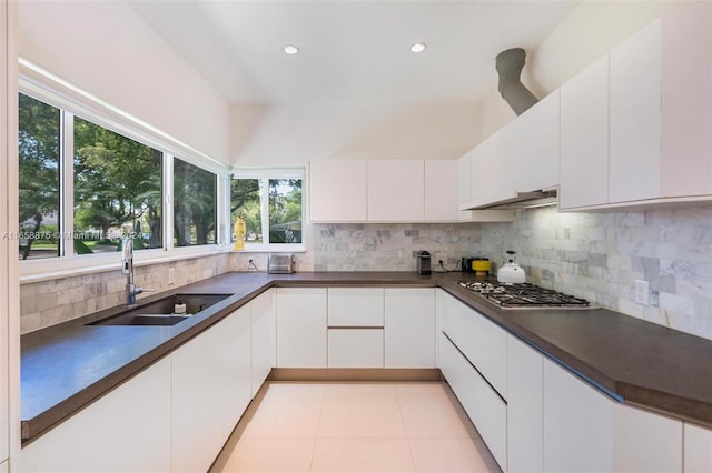 kitchen with stainless steel gas stovetop, white cabinets, sink, light tile patterned floors, and tasteful backsplash