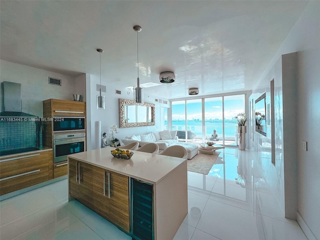 kitchen featuring wall chimney range hood, light tile patterned flooring, a kitchen island, stainless steel oven, and black microwave