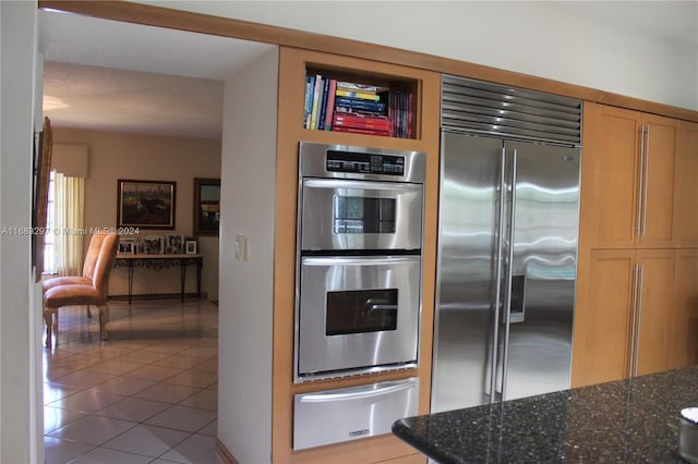 kitchen with appliances with stainless steel finishes, tile patterned floors, and dark stone counters