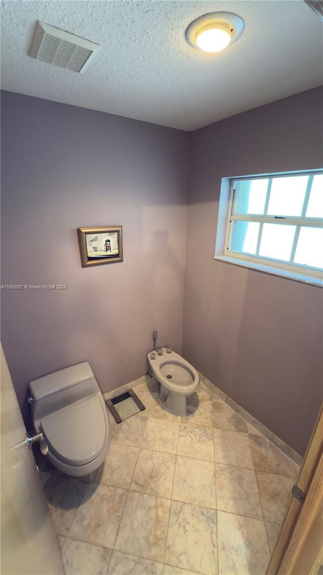 bathroom featuring toilet, a textured ceiling, and a bidet