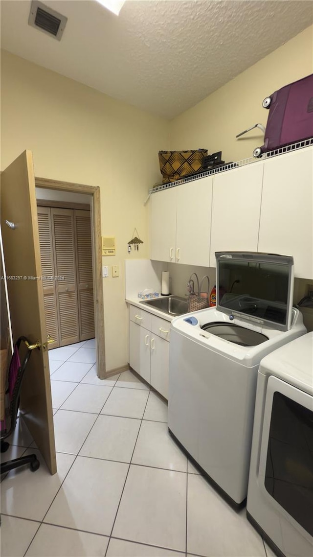 clothes washing area featuring cabinets, light tile patterned floors, a textured ceiling, washing machine and dryer, and sink