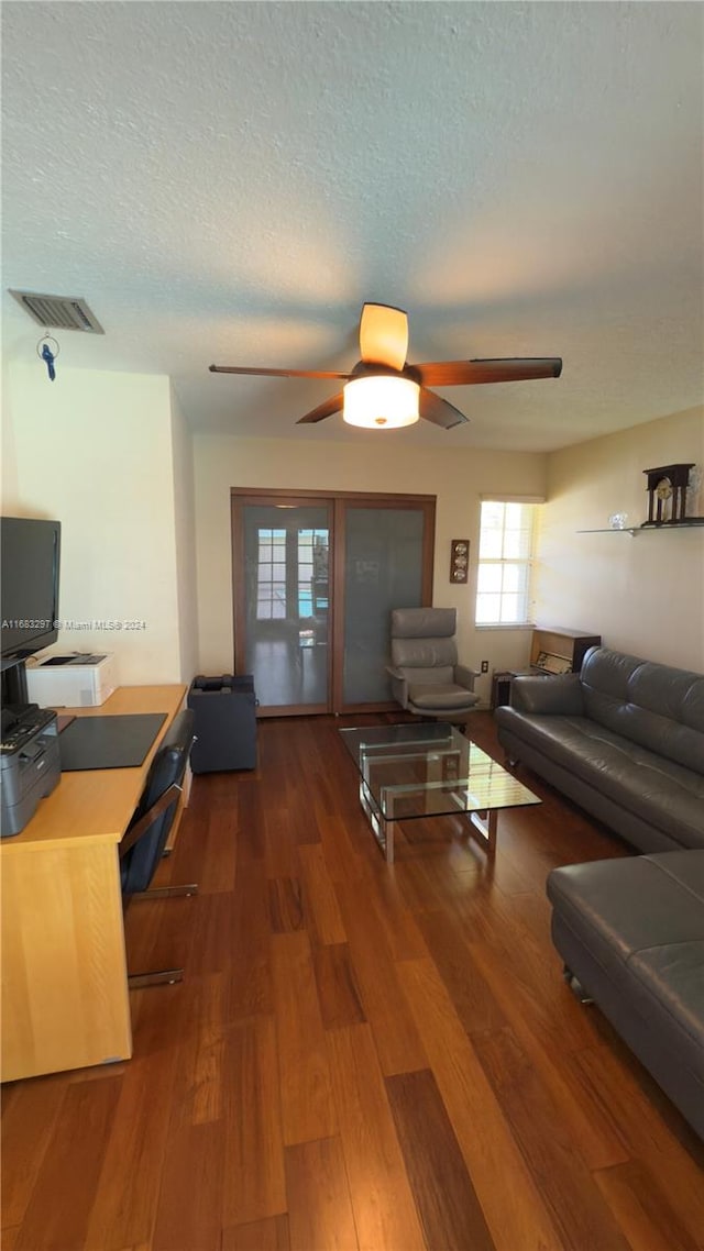 living room featuring dark wood-type flooring, ceiling fan, and a textured ceiling