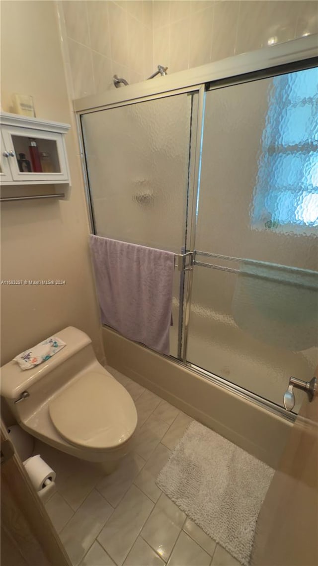 bathroom with toilet, shower / bath combination with glass door, and tile patterned flooring