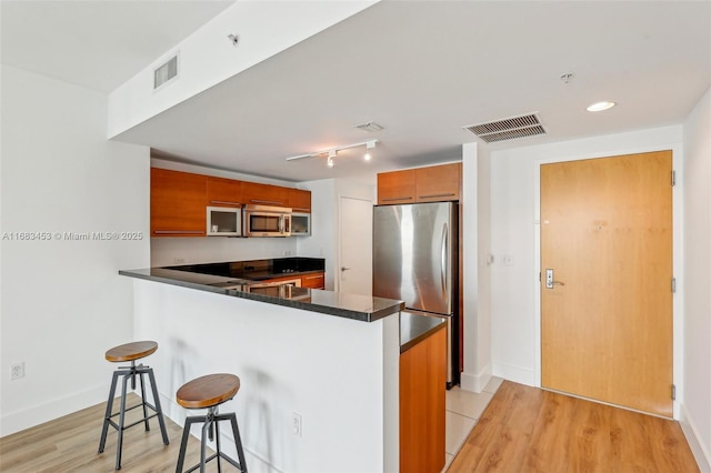 kitchen featuring kitchen peninsula, light hardwood / wood-style flooring, a breakfast bar, and stainless steel appliances