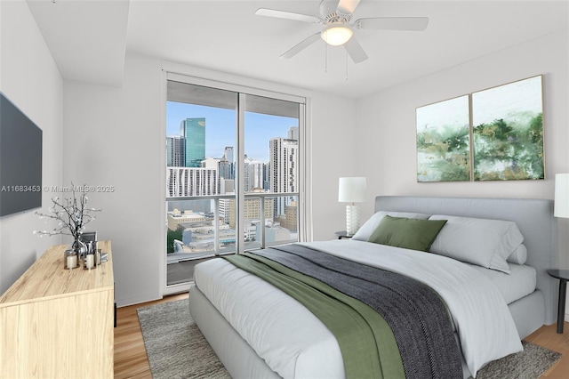 bedroom with hardwood / wood-style flooring, a wall of windows, and ceiling fan