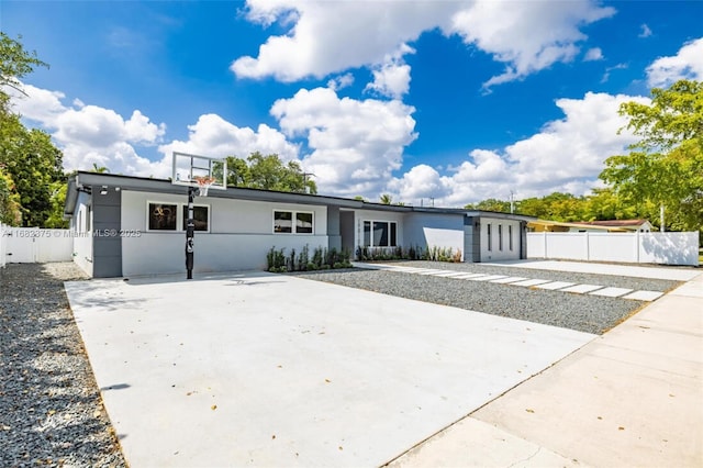 view of front facade featuring driveway, stucco siding, fence, and basketball court