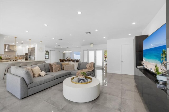 kitchen with wall chimney range hood, appliances with stainless steel finishes, white cabinetry, hanging light fixtures, and light stone countertops