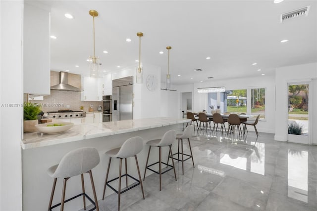 kitchen featuring decorative light fixtures, visible vents, appliances with stainless steel finishes, white cabinets, and wall chimney range hood