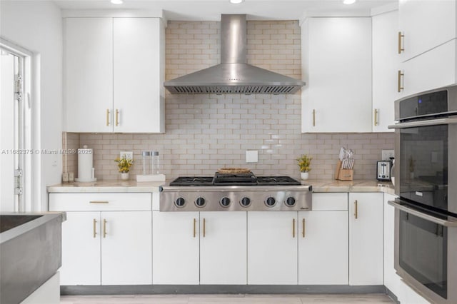 kitchen with white cabinets, wall chimney range hood, stainless steel appliances, and decorative backsplash