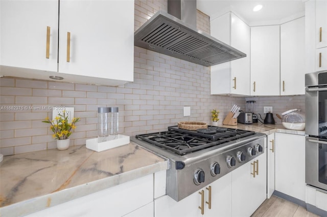 kitchen featuring stainless steel appliances, white cabinetry, ventilation hood, and light stone counters