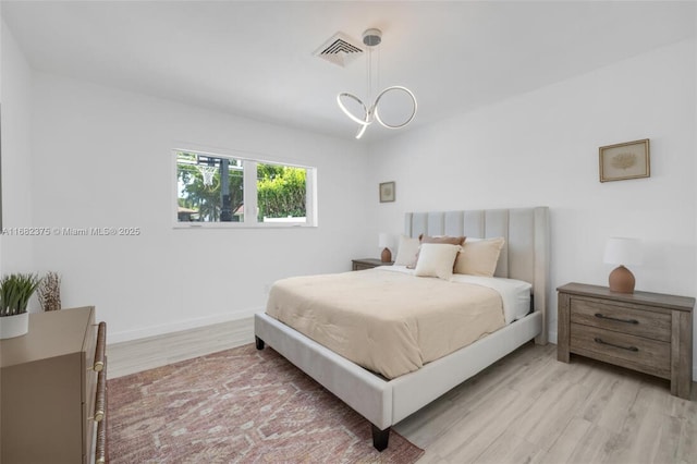 bedroom featuring visible vents, a notable chandelier, light wood-style flooring, and baseboards