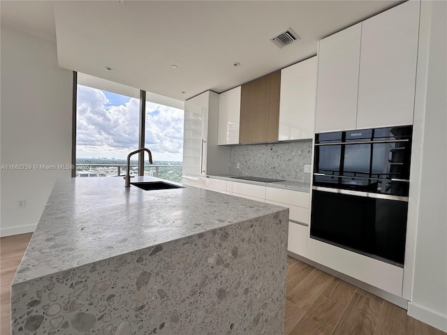 kitchen featuring sink, light hardwood / wood-style floors, white cabinetry, and light stone countertops