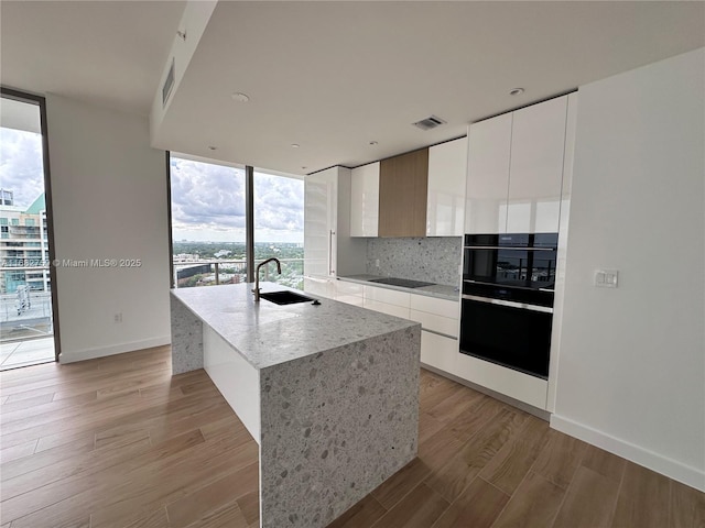 kitchen featuring white cabinetry, sink, light wood-type flooring, and a wall of windows