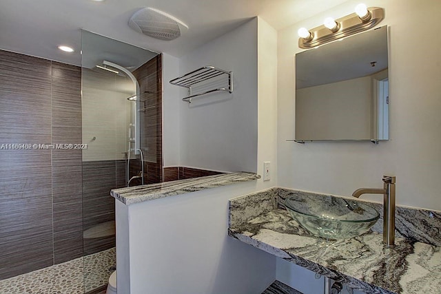 bathroom with a tile shower, toilet, and sink