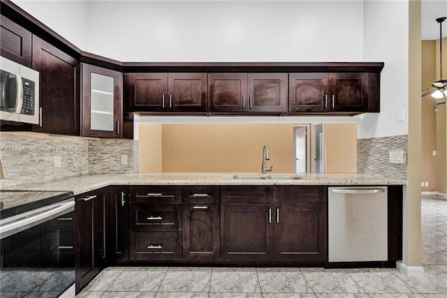 kitchen featuring light stone countertops, backsplash, dark brown cabinets, stainless steel appliances, and sink