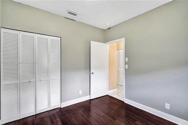 unfurnished bedroom with a textured ceiling, a closet, and dark hardwood / wood-style floors