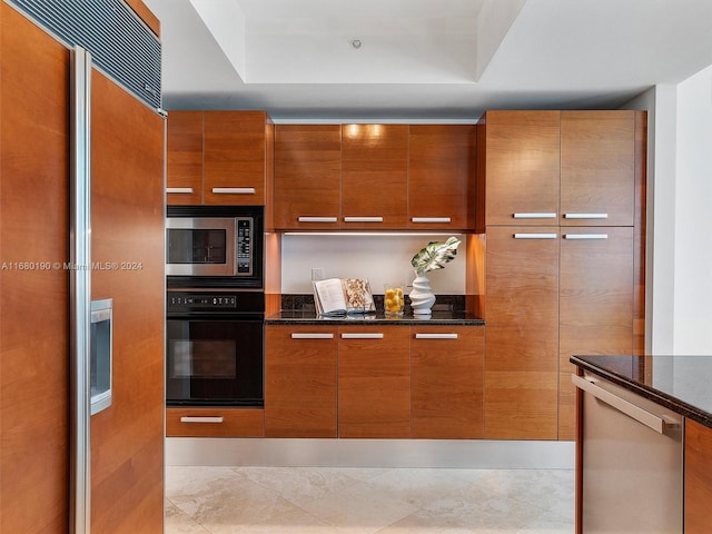 kitchen featuring built in appliances, a tray ceiling, and dark stone countertops