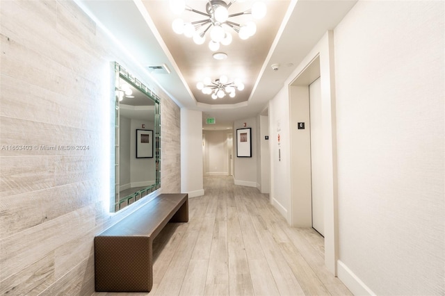 hall with a raised ceiling, elevator, a chandelier, and light hardwood / wood-style floors