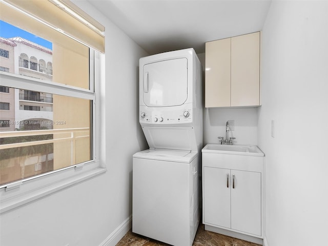 clothes washing area with cabinets, stacked washer / dryer, and sink