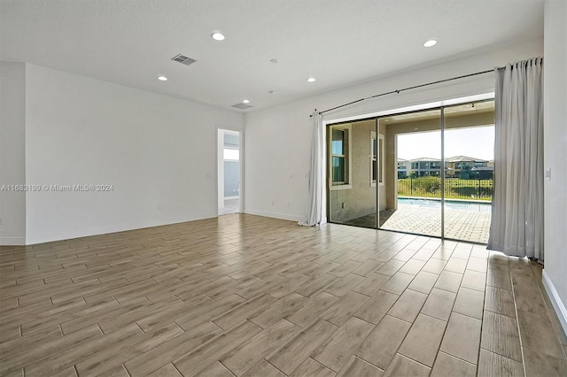 unfurnished room with light hardwood / wood-style flooring and a textured ceiling