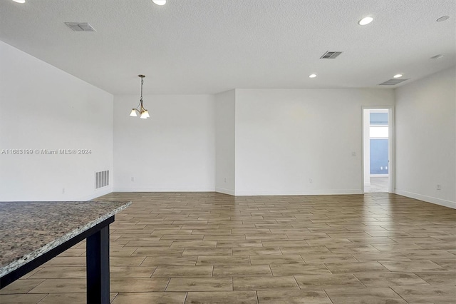 empty room with an inviting chandelier, a textured ceiling, and light hardwood / wood-style floors