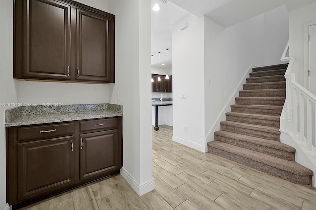 kitchen with light stone countertops, dark brown cabinets, and light hardwood / wood-style flooring