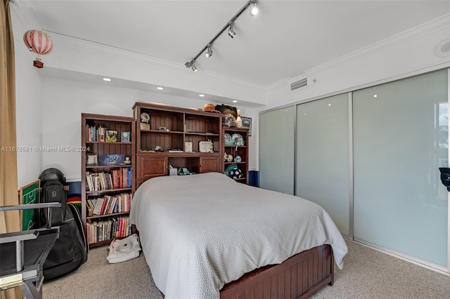 bedroom featuring a closet, rail lighting, carpet flooring, and crown molding