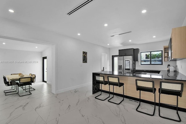 kitchen featuring sink, light brown cabinets, stainless steel fridge with ice dispenser, kitchen peninsula, and a kitchen bar