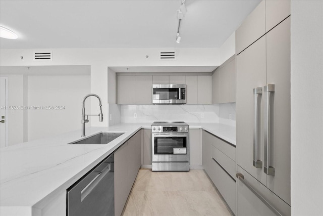 kitchen with track lighting, light stone counters, appliances with stainless steel finishes, gray cabinetry, and sink