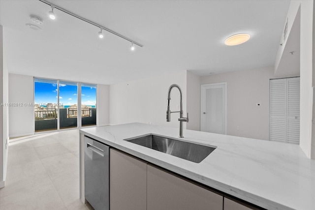 kitchen featuring light stone counters, rail lighting, expansive windows, stainless steel dishwasher, and sink