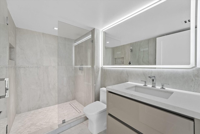 bathroom featuring toilet, a shower with shower door, vanity, and tile walls