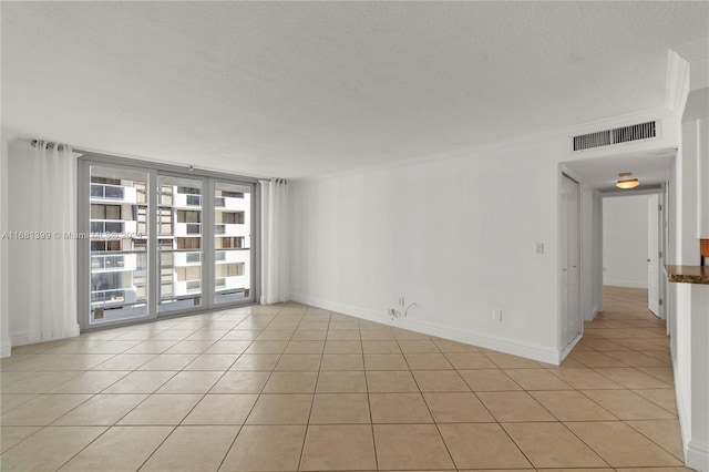 empty room with a textured ceiling, baseboards, light tile patterned floors, visible vents, and ornamental molding