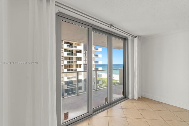 tiled spare room featuring a textured ceiling, a water view, and a beach view